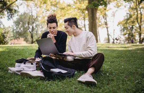 Two students on a computer outside on the lawn