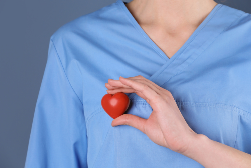 Person in scrubs holding a red stressball heart over their heart